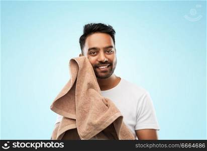 grooming and people concept - smiling indian man with bath towel drying his face over blue background. smiling indian man with towel over blue background