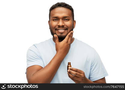 grooming and people concept - smiling young african american man applying lotion or beard oil over white background. african man applying grooming oil to beard