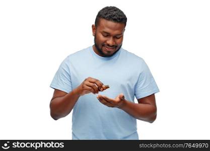 grooming and people concept - smiling young african american man applying lotion or beard oil over white background. african man applying grooming oil to beard