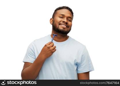 grooming and people concept - smiling young african american man shaving beard with manual razor blade over white background. smiling african man shaving beard with razor blade