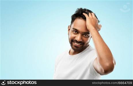 grooming and people concept - smiling young indian man touching his hair over blue background. indian man touching his hair over gray background