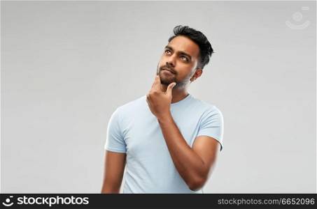 grooming and people concept - thoughtful indian man touching his beard and looking up over grey background. indian man thinking and looking up
