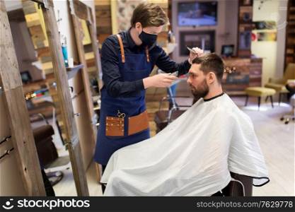 grooming, hairdressing and health safety concept - man and barber or hairdresser wearing face protective medical mask for protection from virus disease with trimmer and comb cutting hair at barbershop. man and barber with trimmer cutting hair at salon