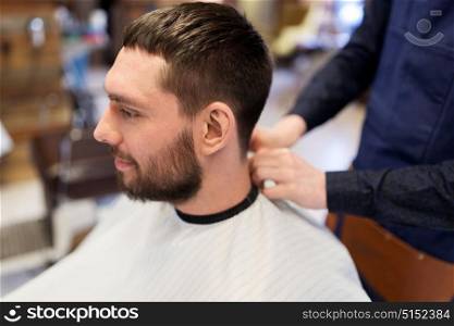 grooming, hairdressing and people concept - hairdresser or barber and man in cape with beard at barbershop. hairdresser and man with beard at barbershop