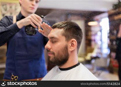 grooming, hairdressing and people concept - hairstylist applying hair styling spray or water to male customer at barbershop. barber applying styling spray to male hair
