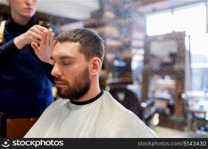 grooming, hairdressing and people concept - hairstylist applying hair styling spray or water to male customer at barbershop. barber applying styling spray to male hair