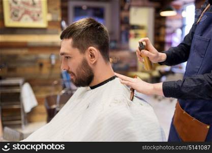 grooming, hairdressing and people concept - hairstylist applying hair styling spray to male customer at barbershop. barber applying styling spray to male hair at shop