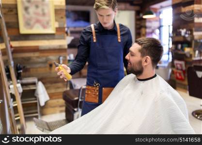 grooming, hairdressing and people concept - hairstylist showing hair styling spray to male customer at barbershop. barber showing hair styling spray to male customer