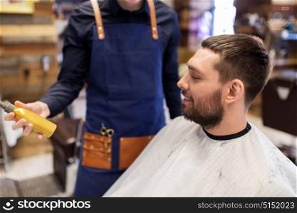 grooming, hairdressing and people concept - hairstylist showing hair styling spray to male customer at barbershop. barber showing hair styling spray to male customer