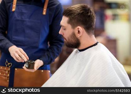 grooming, hairdressing and people concept - hairstylist showing hair styling wax to male customer at barbershop. barber showing hair styling wax to male customer