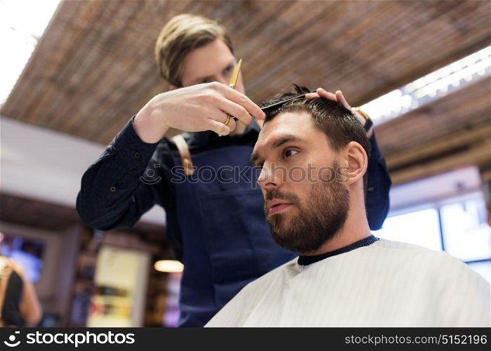grooming, hairdressing and people concept - man and barber with comb and scissors cutting hair at barbershop. man and barber cutting hair at barbershop