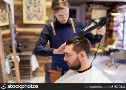 grooming, hairdressing and people concept - man and hairstylist or barber with fan drying hair at barbershop. barber with fan drying male hair at barbershop