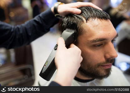 grooming, hairstyle and people concept - man and barber or hairdresser hands with trimmer cutting hair at barbershop. man and barber hands with trimmer cutting hair