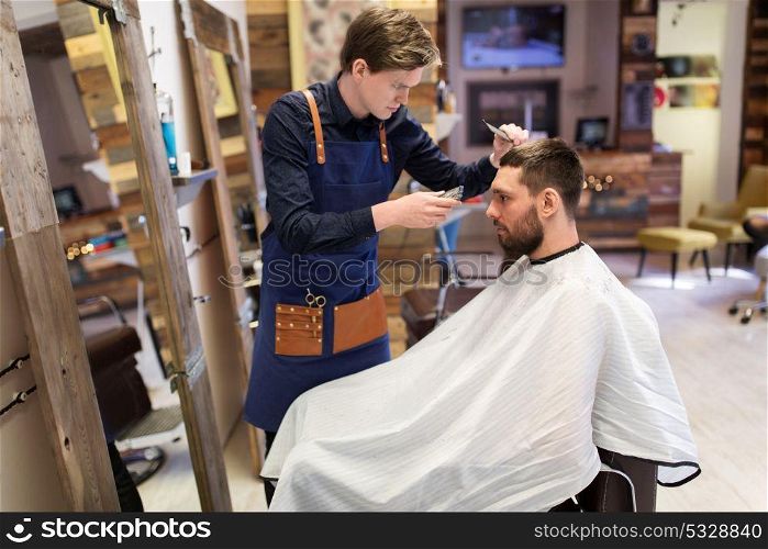 grooming, hairstyle and people concept - man and barber or hairdresser with trimmer and comb cutting hair at barbershop. man and barber with trimmer cutting hair at salon