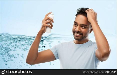 grooming, hairstyling and people concept - happy smiling indian man applying hair spray over blue background with air bubbles or water splash. smiling indian man applying hair spray over gray