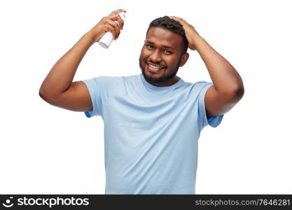 grooming, hairstyling and people concept - smiling young african american man applying hairspray to his hair spray over white background. african american man applying hairspray to hair