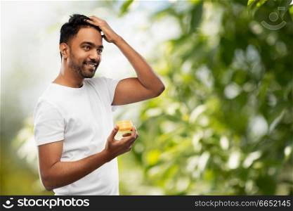 grooming, hairstyling and people concept - smiling young indian man applying hair wax or styling gel over green natural background. indian man applying hair wax or styling gel