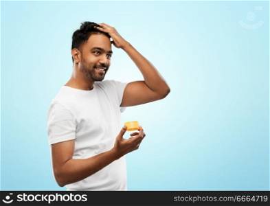 grooming, hairstyling and people concept - smiling young indian man applying hair wax or styling gel over blue background. indian man applying hair wax or styling gel
