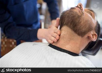 grooming, shaving and people concept - barber treating male client&rsquo;s neck with balm at barbershop. barber treating male client&rsquo;s neck at barbershop