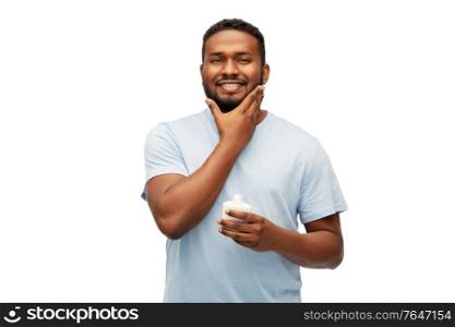 grooming, skin care and people concept - happy african american man applying cream to his face over white background. happy african man applying cream to his face