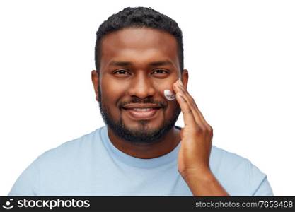 grooming, skin care and people concept - happy smiling african american applying moisturizer to his face over white background. african american man applying moisturizer to face