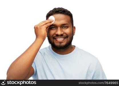 grooming, skin care and people concept - young african american man cleaning his face with cotton pad over white background. african american man cleaning face with cotton pad