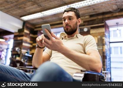 grooming, technology and people concept - man with smartphone at barbershop or hairdressing salon. man with smartphone at barbershop or salon