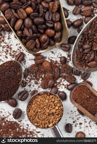 Ground and bean coffee and freeze dried instant coffee granules in various spoons and scoops on white background. Top view