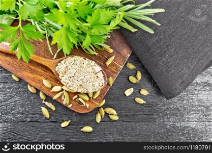Ground cardamom in a spoon, seasoning capsules, napkin, fresh parsley and rosemary on a wooden board background from above
