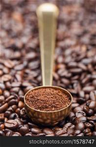 Ground coffee in golden steel scoop on fresh coffee beans background. Macro