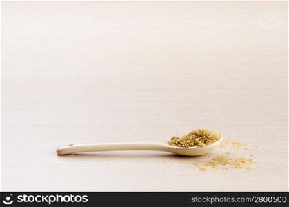 Ground Coriander in a spoon with some spilt over the wooden background