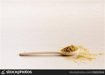 Ground Cumin in a spoon with some spilt over the wooden background