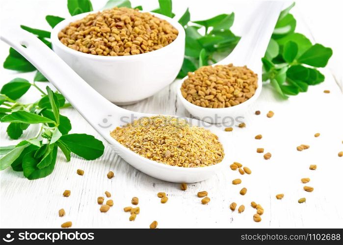 Ground fenugreek in a spoon, spice seeds in a bowl and spoon with leaves on wooden board background