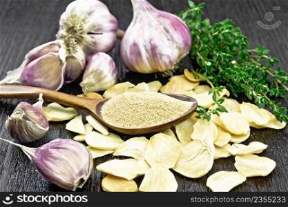 Ground garlic in a spoon, dried and fresh garlic, bunch of thyme on dark wooden board background