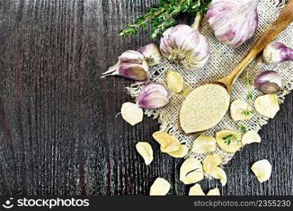 Ground garlic in a spoon on a burlap, dried and fresh garlic, bunch of thyme on background of wooden board from above