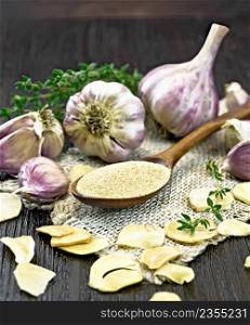 Ground garlic in a spoon on a burlap napkin, dried and fresh garlic, bunch of thyme on background of wooden board