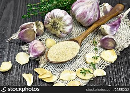 Ground garlic in a spoon on burlap, dried and fresh garlic, a bunch of thyme on dark wooden board background