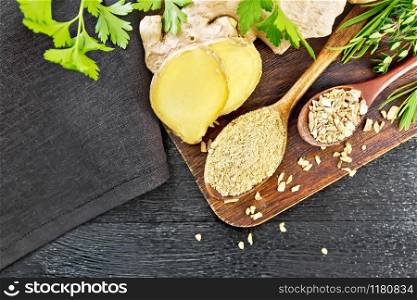 Ground ginger and flakes in two wooden spoons, ginger root, spicy herbs, napkin on a wooden board background from above