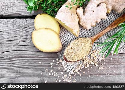 Ground ginger in a spoon, flakes and ginger root on burlap, spicy herbs on a wooden board background from above