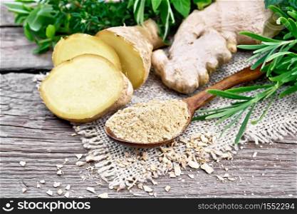 Ground ginger in a spoon, flakes and ginger root on burlap, spicy herbs on a background of an old wooden board