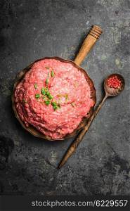 Ground meat in cooking pan with wooden spoon and spices on dark rustic background, top view composing.