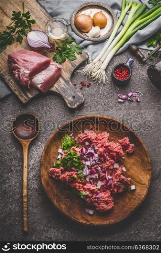 Ground meat in plate with cooking spoon with ingredients on rustic kitchen table background, top view
