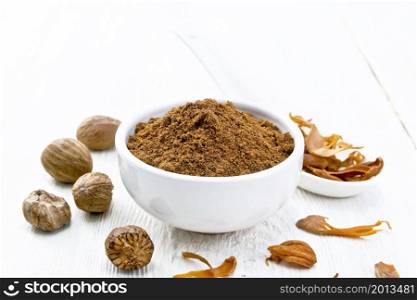 Ground nutmeg in a bowl and dried nutmeg arillus in a spoon, whole nuts on wooden board background