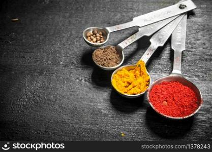 Ground spices in measuring spoons. On the black chalkboard.. Ground spices in measuring spoons.