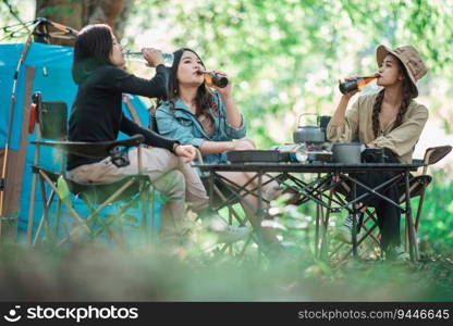 Group beautiful Asian women friends travelers  relaxing at front of c&ing tent, They enjoy to talking and drinking beer with fun and happy together