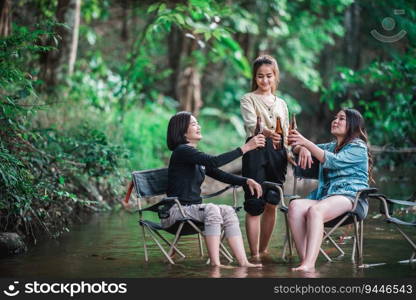 Group beautiful Asian women friends travelers relaxing in c&chairs  in stream, They are cheering and drinking beer during c&ing, talking with fun and happy together