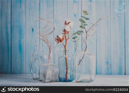 Group decorative branches in glass bottles on wooden background. Composition with decorative branches
