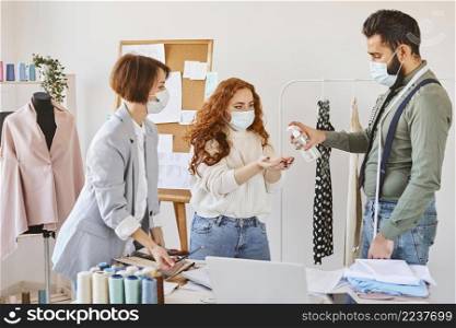 group fashion designers with medical masks disinfecting hands while working atelier