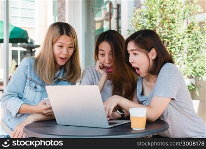 Group happy asian women friends watching media content on line in laptop sitting in coffee shop. Happy asian women friends giving laptop gift to surprised girl in coffee shop. Shopping online concept.
