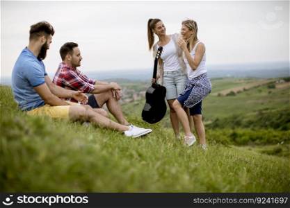 Group od young people sitting on grass and having fun on a field trip in nature on a mountain